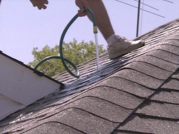 Worker repairing a shingled roof with a green hose on a sunny day