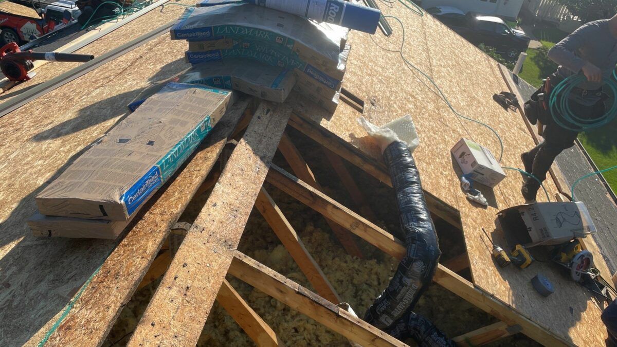 Roof construction site with exposed wooden trusses, blue materials, and tools scattered on plywood decking
