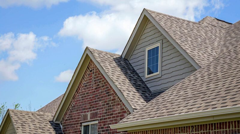 Brick-and-siding house roof with gables and a dormer window under a blue sky
