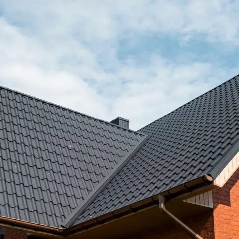 Dark gray tiled roof on a brick house under a partly cloudy sky