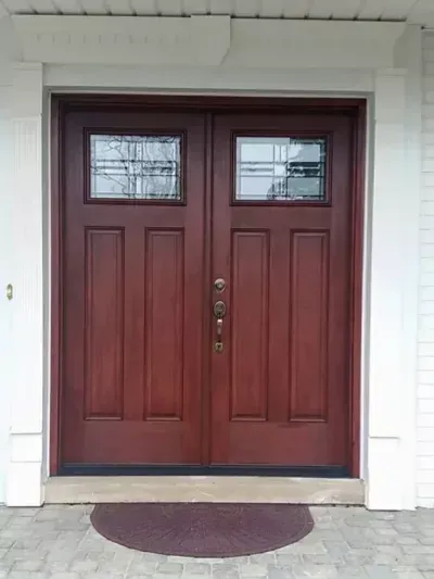 Front entrance with dark red double doors, small windows, and a semicircular doormat
