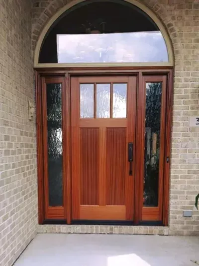 Wooden front door with arched transom and sidelights set in a brick entryway.