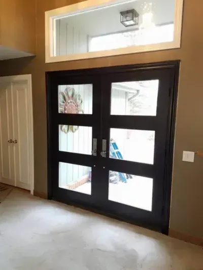 Indoor entryway with a dark-framed glass door and sidelights, beige walls, and a small window above.