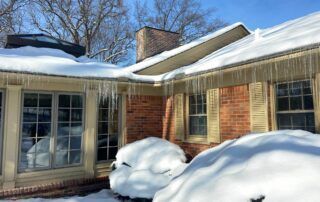 Snow-covered brick house with large windows and a chimney on a sunny winter day