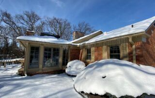 Snow-covered house with large drifts in the yard on a sunny winter day