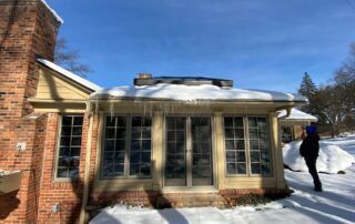 Snow-covered sunroom attached to a brick house, with a person standing outside by the windows.