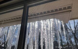 Icicles hanging from a roof edge above a window with tree branches in the background
