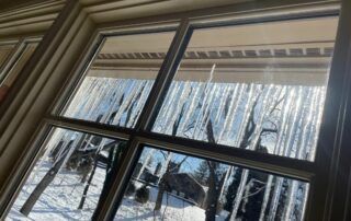 Snowy yard seen through a window with icicles hanging from the roof eaves