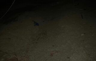 Dimly lit dirt ground with a small blue object near the center and a few dark debris spots.