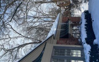 Snow-covered brick house with white-trimmed windows and bare trees in winter