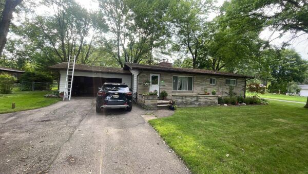 Single-story stone house with a car parked in the driveway and a carport on the left.