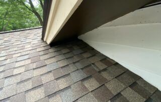 Close-up of gray asphalt roof shingles beside white soffit and beige trim under a roof edge