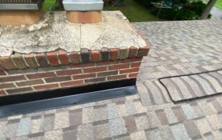 Brick chimney and rooftop flashing on a shingled roof with a paver walkway nearby