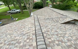 Roof shingles viewed from the ridge, with a pickup truck and trees in the background