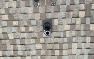 Close-up of a shingled roof with a small black vent or pipe in the center.