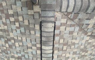 Close-up of a patterned shingle roof with a central metal vent pipe.