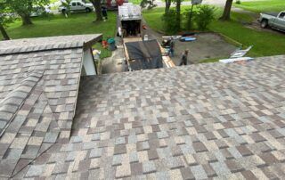Shingled roof with a gray stone tile pattern, overlooking a driveway and green yard below.