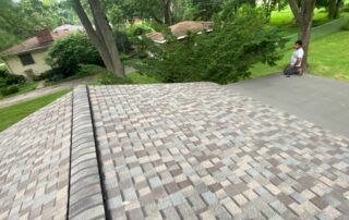 Brick-paved walkway beside a road, with a person sitting near trees and a house in the background