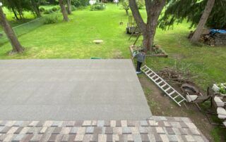 Backyard patio with gray pavers, green lawn, trees, and a ladder near the side of the house