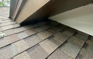Roof shingles meeting a dormer wall with dark water damage along the seam