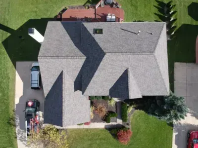 Aerial view of a gray-roofed house with a driveway, parked vehicles, and a landscaped yard