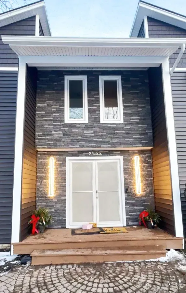 Front entrance of a modern house with brick facade, white trim, double doors, and warm porch lights