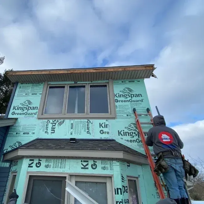 Worker on ladder installing green Kingspan insulation panels on a house exterior under construction