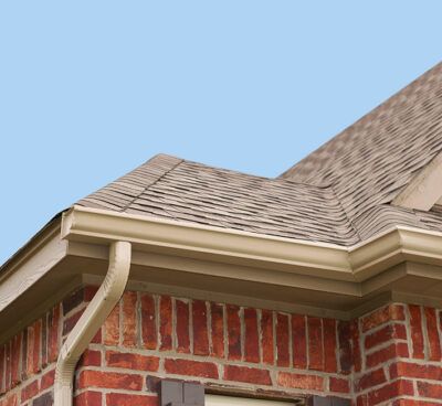 Close-up of a brick house roof with beige gutters and a blue sky background