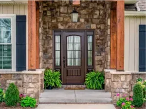 Front porch with stone columns, wooden front door, and potted green plants on either side.