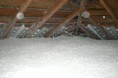 Snow piled in an attic beneath exposed wooden rafters and hanging light bulbs