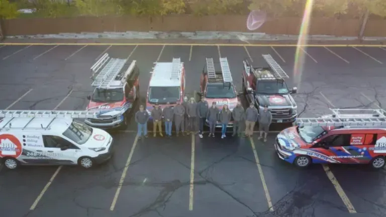 Four utility trucks and a van parked in a lot, with people standing in a line between them.