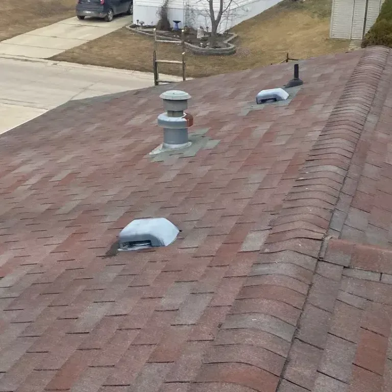 Rooftop with red shingles, two vents, and a small black pipe near a driveway.