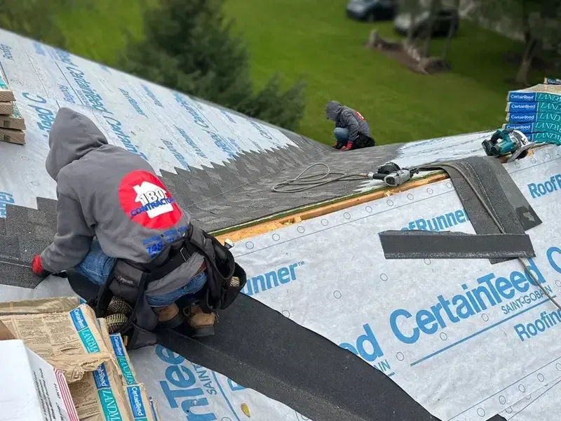 Workers install roofing shingles on a pitched roof covered with CertainTeed underlayment above a grassy yard.