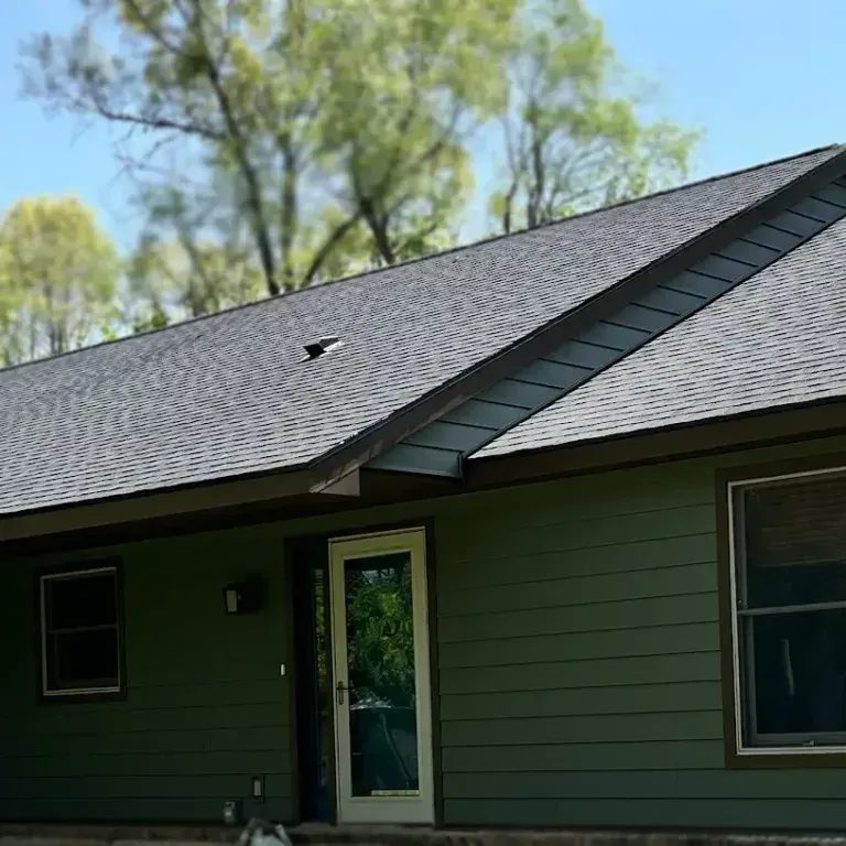 Green house exterior with dark roof, windows, and a white-framed door under blue sky.