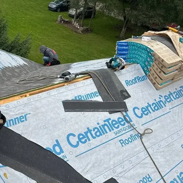Roofing workers on a gray roof installing CertainTeed underlayment near stacked shingles