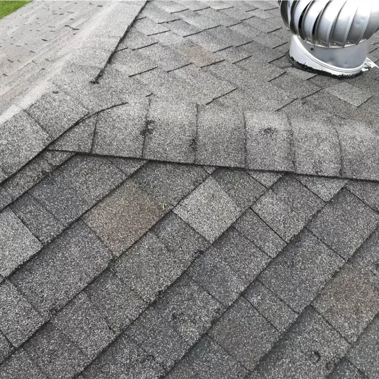 Gray shingled roof with a metal vent pipe and patchwork repairs