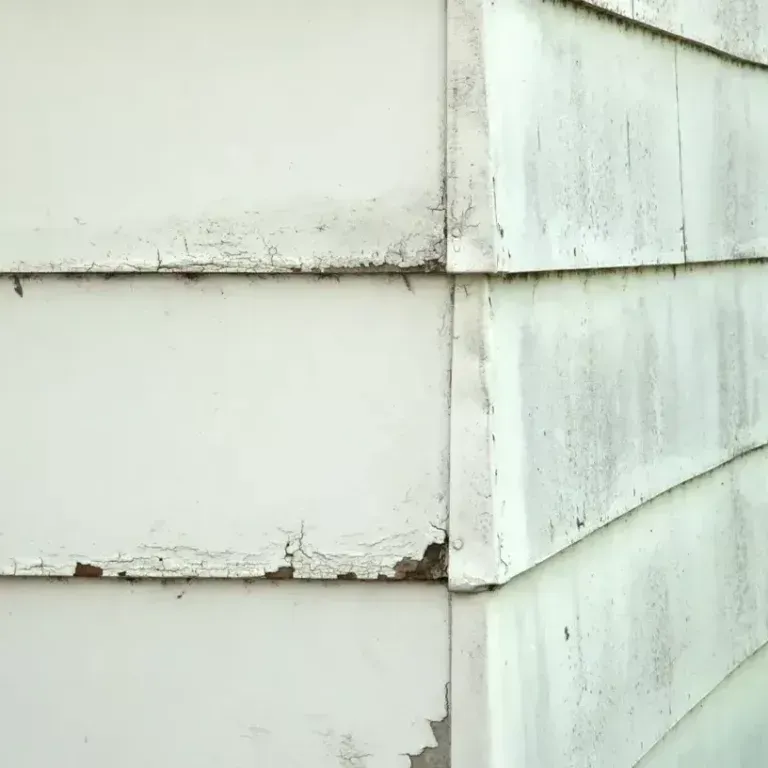 Close-up of a white house corner with peeling paint and weathered siding.