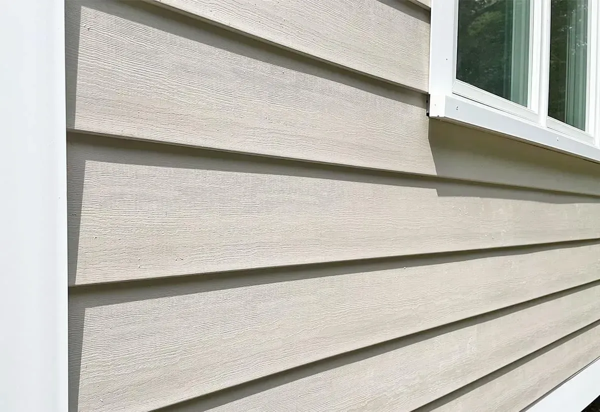 Close-up of beige vinyl house siding with a white-framed window edge.