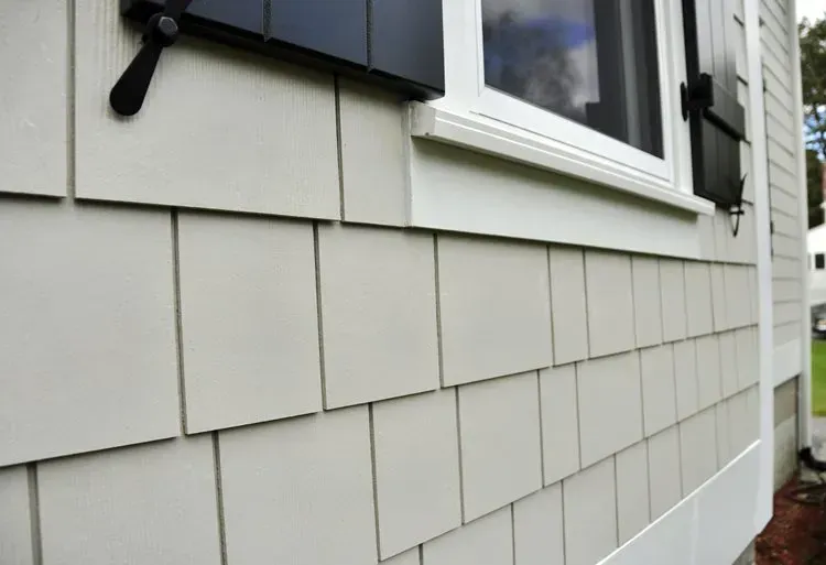 Close-up of light gray house siding with a white-trimmed window and black exterior light fixture