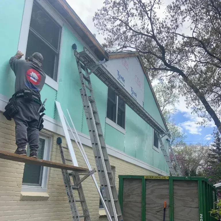 Workers on ladders repairing the exterior of a mint-green two-story building