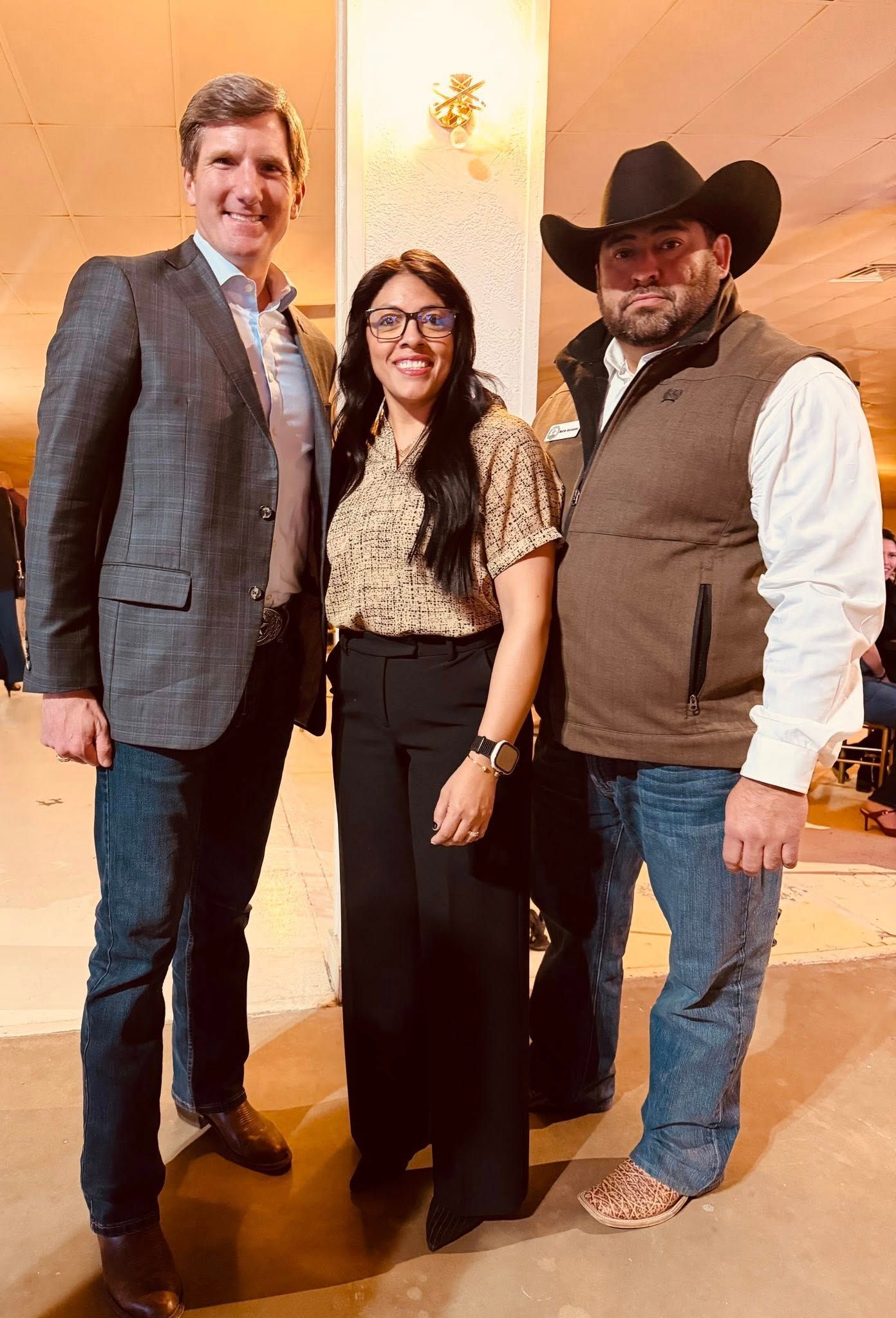 Three people posing indoors, dressed in business and western attire, smiling at the camera.