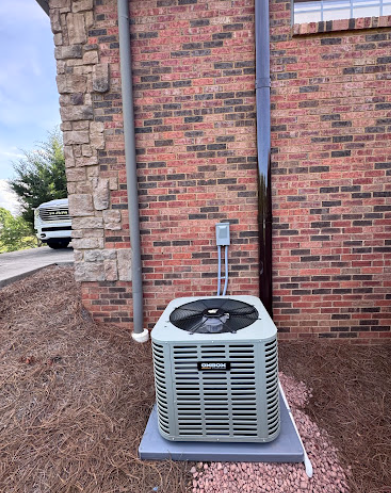 Outdoor HVAC unit beside a brick building wall, with stone siding and a parked white vehicle in the background