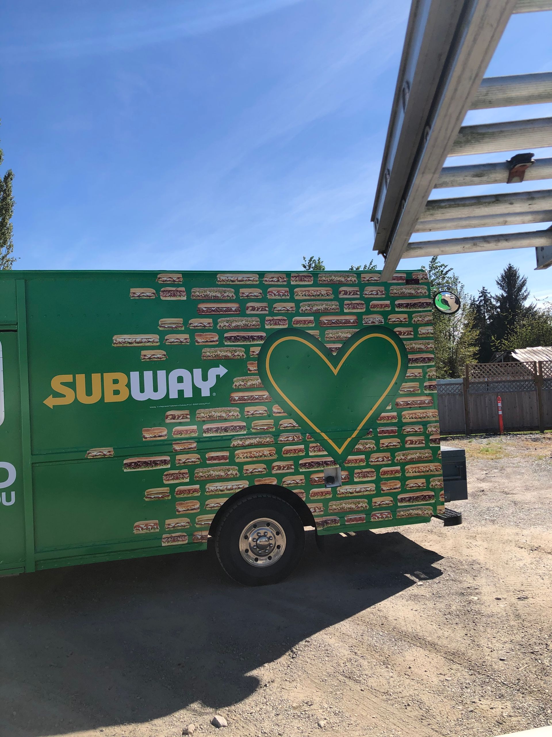 A green subway truck with a heart on the side is parked in a parking lot.