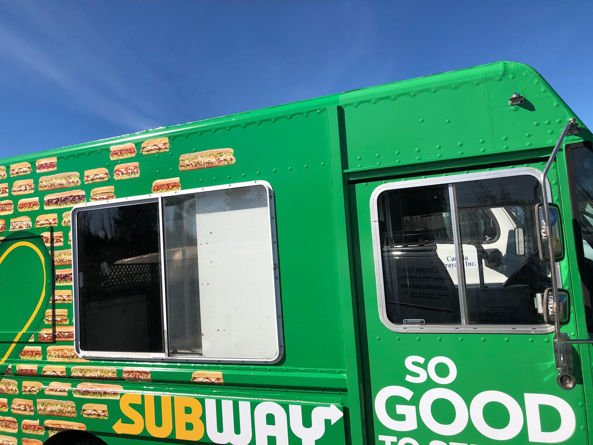 A green subway food truck is parked in front of a blue sky