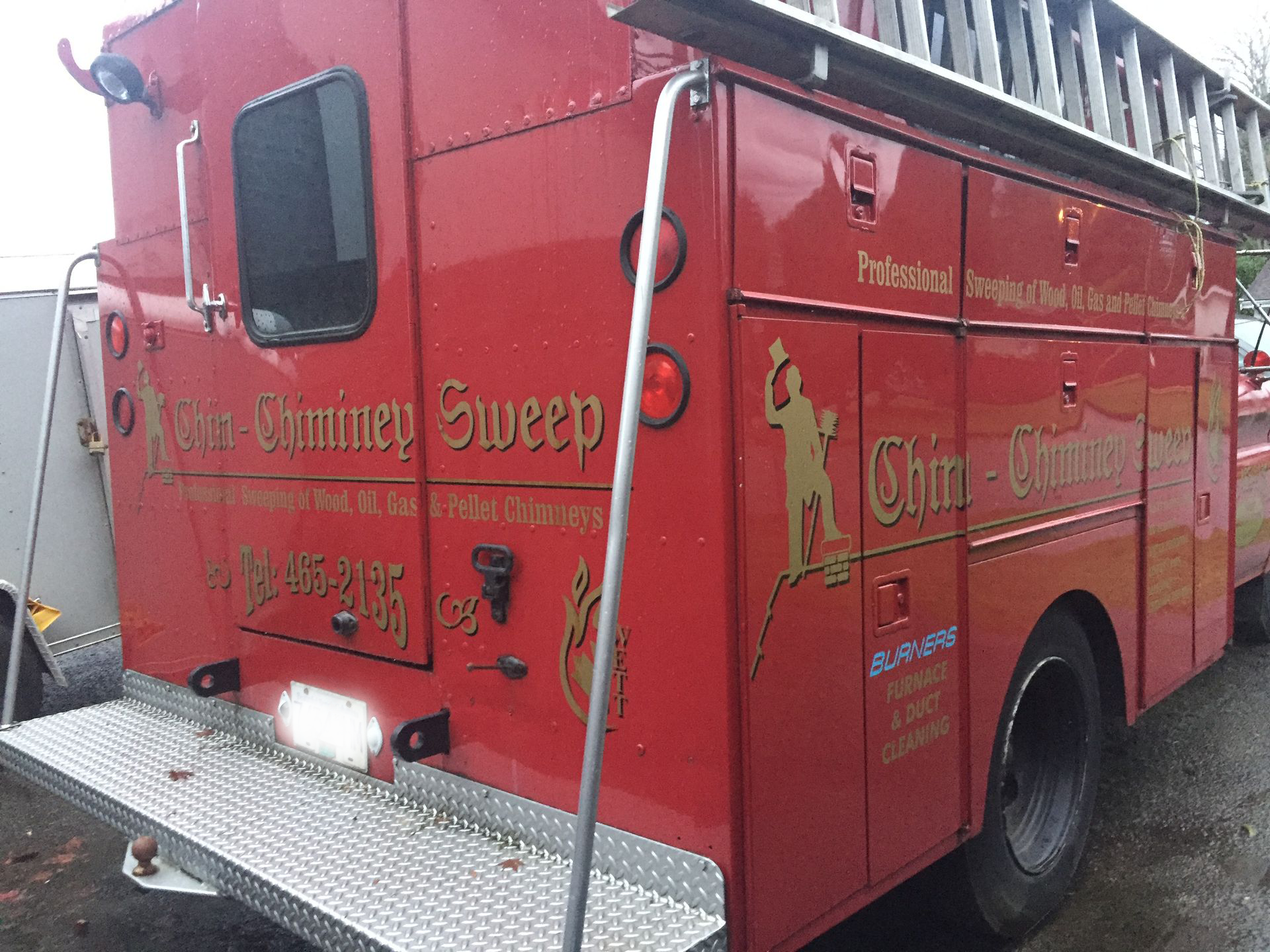 A red chimney sweep truck is parked on the side of the road