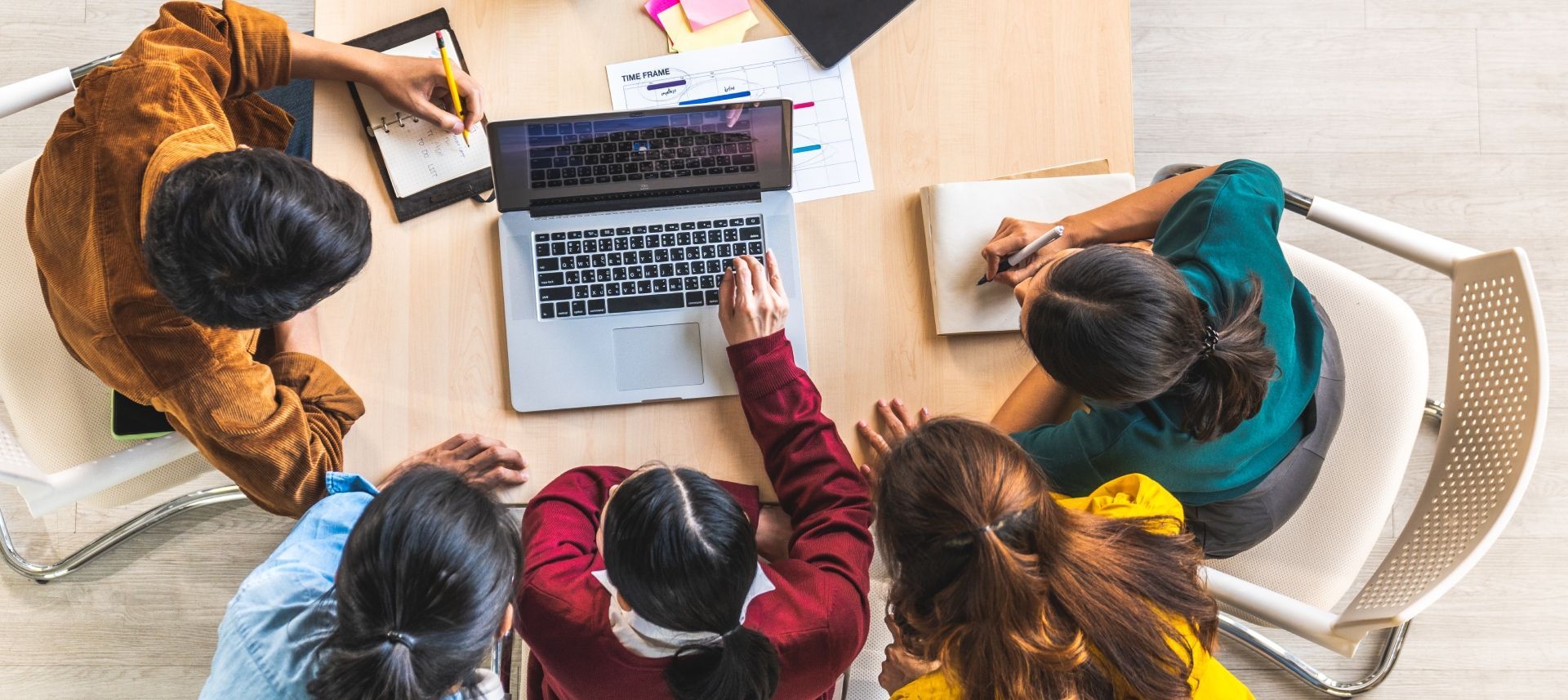 A group of people are sitting around a table looking at a laptop computer.
