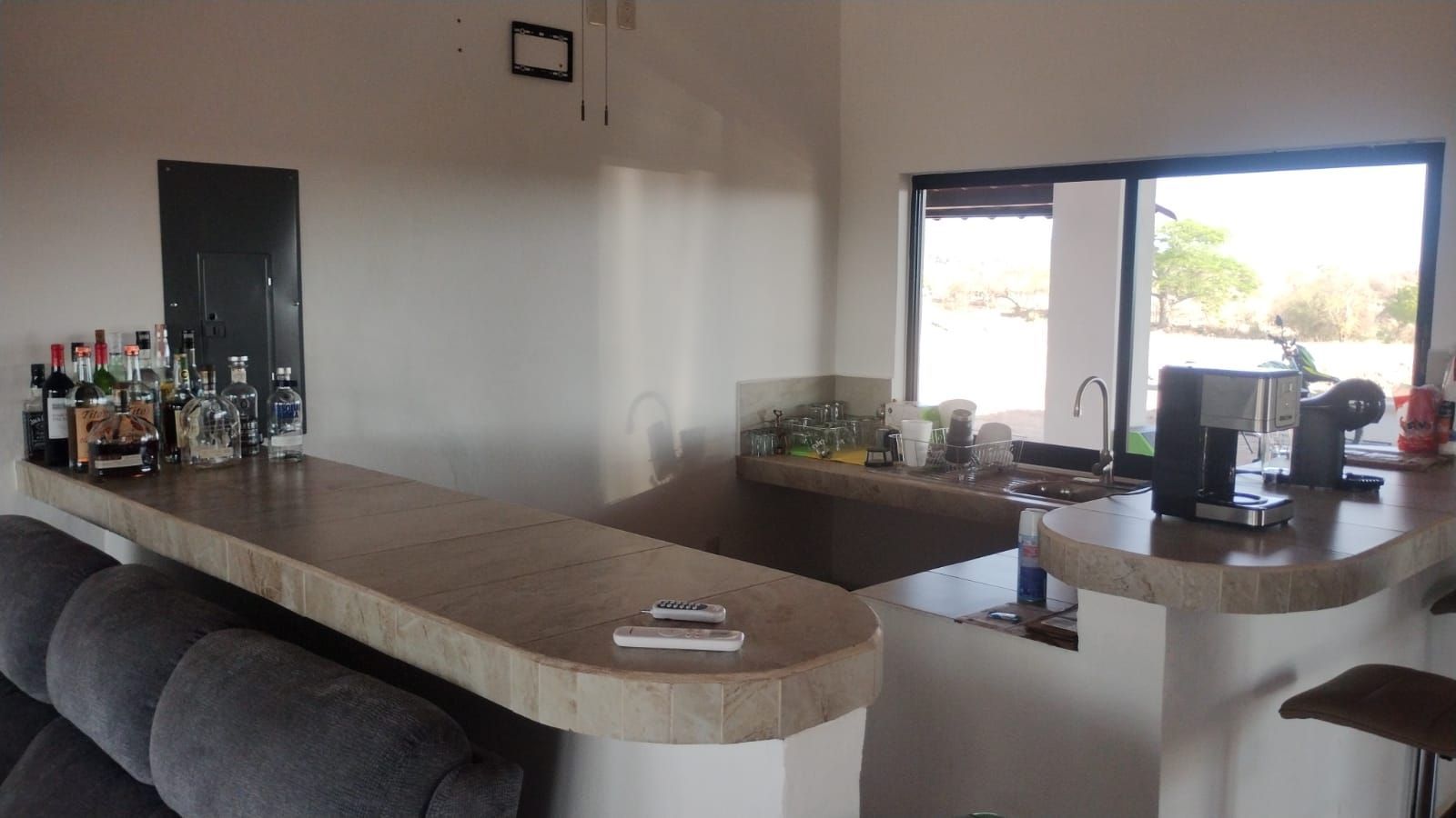 Modern kitchen with a long counter, stools, wine bottles, and an open window to the outside.