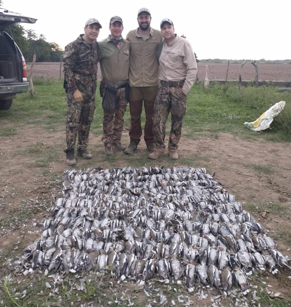 Four hunters stand behind a large pile of caught fish on a dirt field.