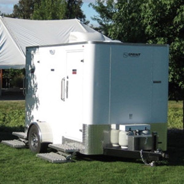 White enclosed trailer with side door and equipment, parked on grass near trees and a tent.