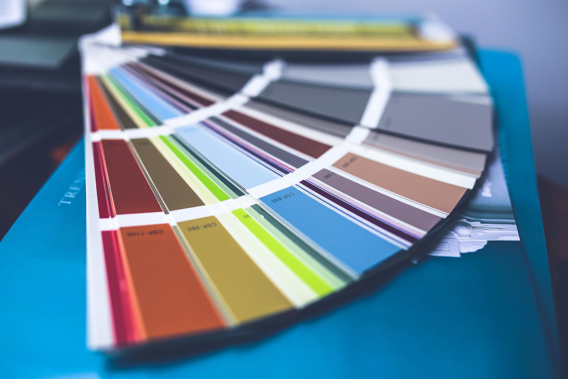 Fan of printed color swatches on a desk, showing rainbow paint samples and neutral tones